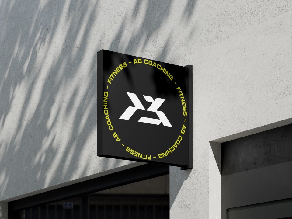 Enseigne drapeau AB Coaching sur une façade blanche, monogramme blanc et lettrage jaune sur fond noir