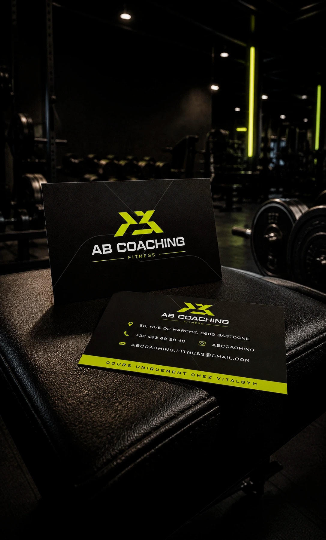 Cartes de visite AB Coaching recto-verso, noir et jaune fluo, posées sur un banc de musculation